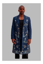 Man wearing a long blue floral coat on a gray background