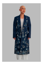 Woman wearing a long blue floral coat against a gray background