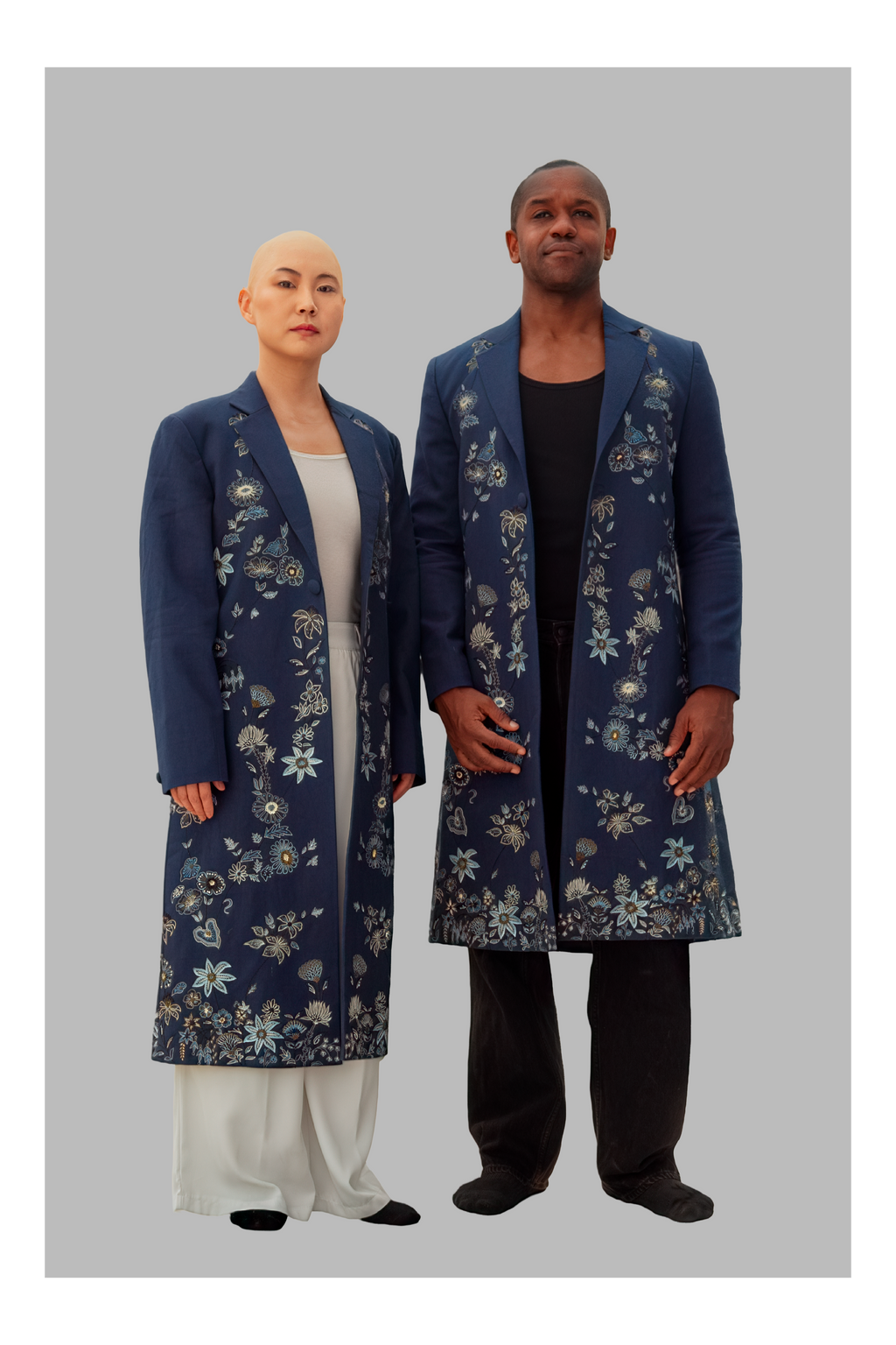 Two people wearing matching blue floral coats on a gray background