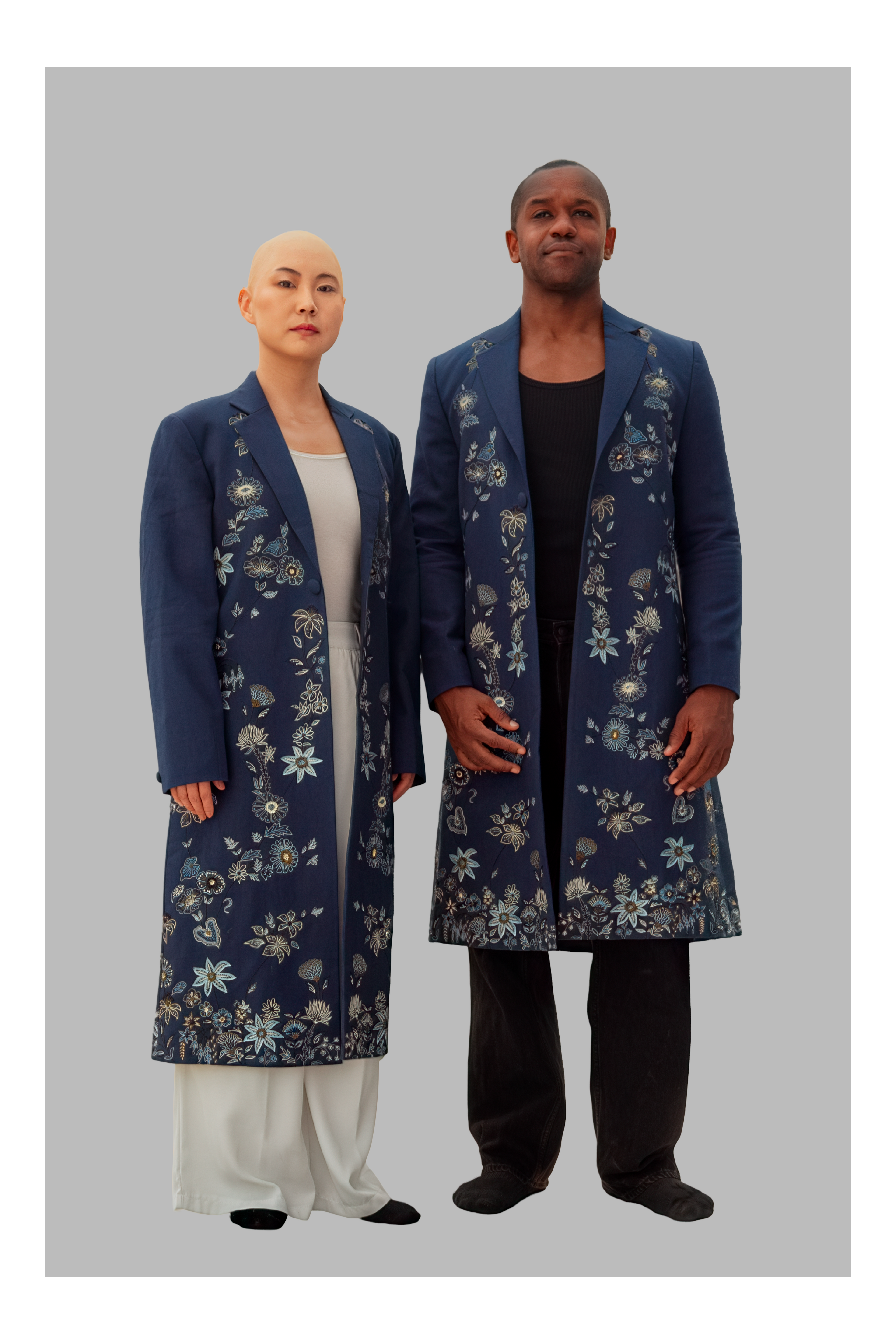 Two people wearing matching blue floral coats on a gray background