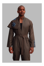 Man wearing a grey jumpsuit with blue accents on a gray background