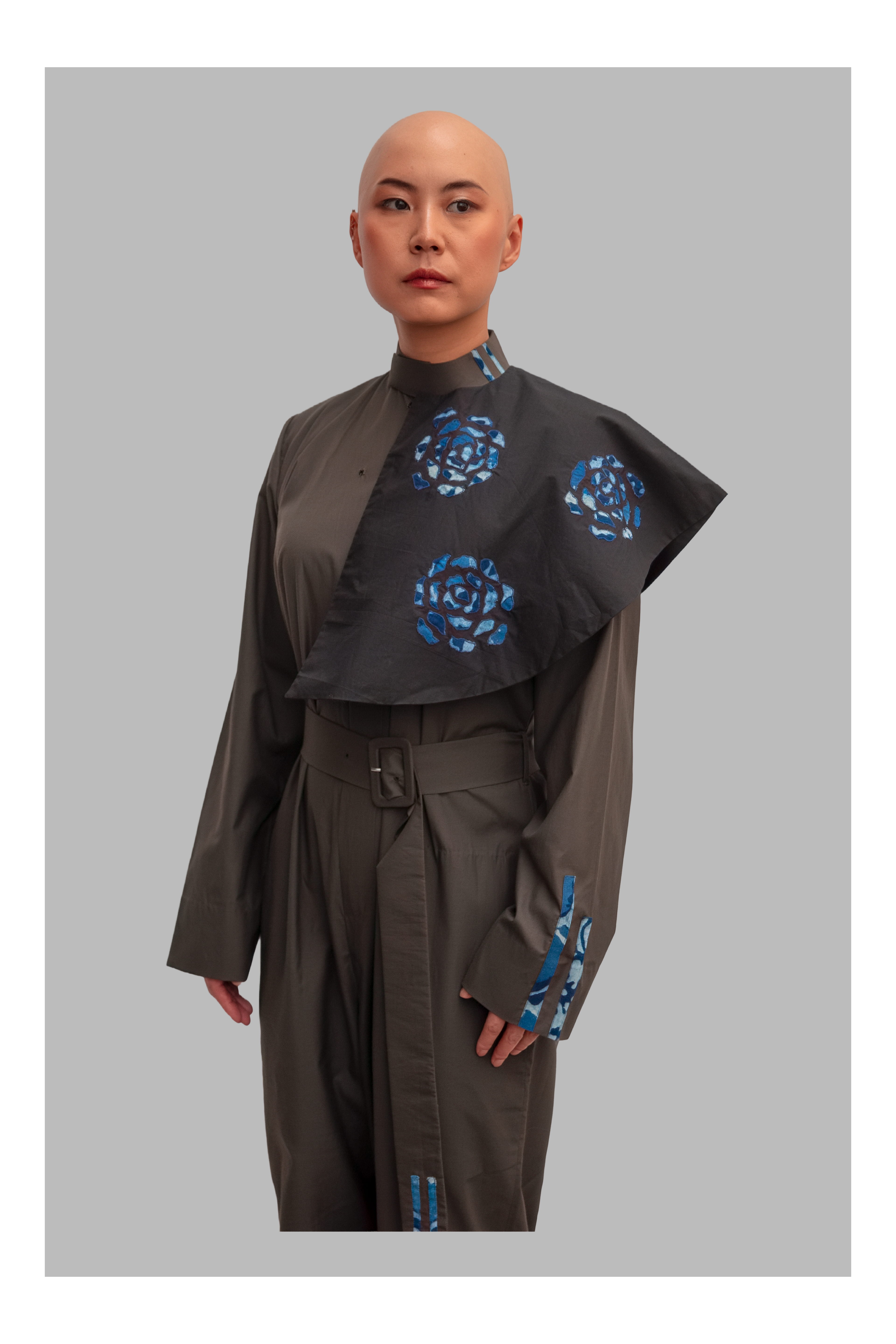female wearing a grey jumpsuit with blue floral patterns on a gray background