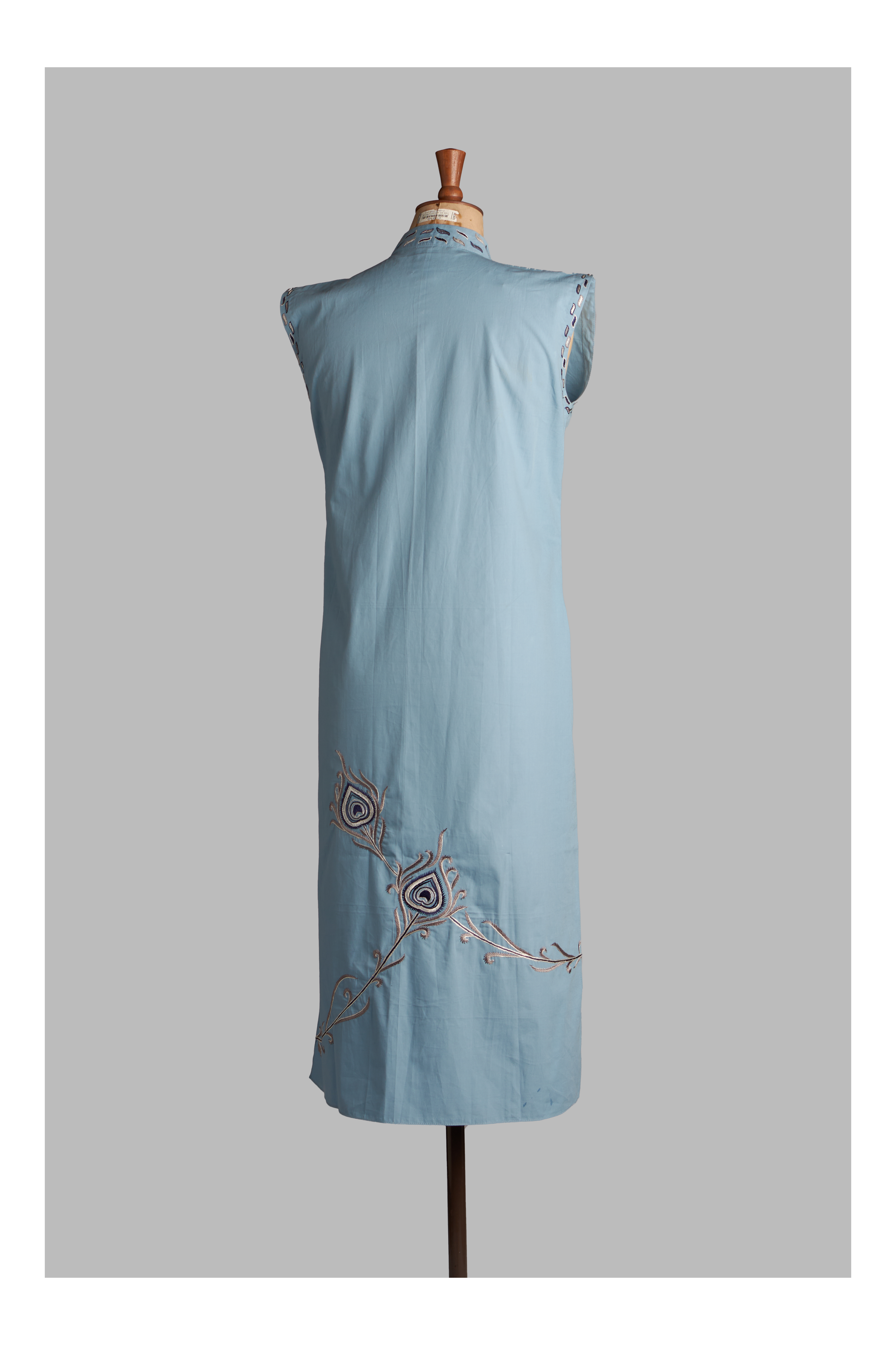 Light blue sleeveless top with peacock embroidery on a mannequin against a gray background
