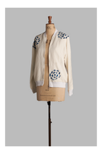 Mannequin wearing a white-colored bomber jacket with blue floral patterns on a gray background