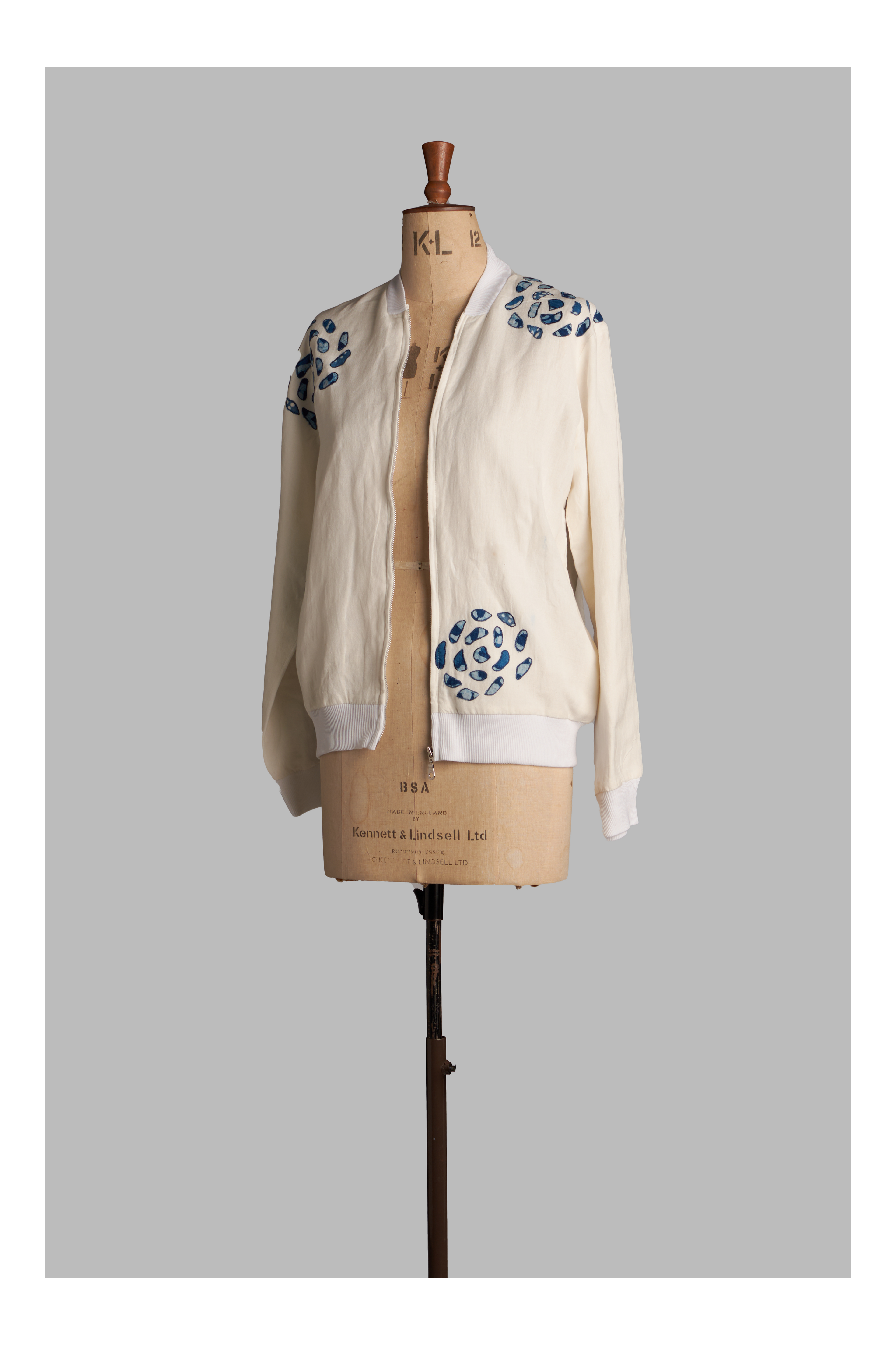 Mannequin wearing a white-colored bomber jacket with blue floral patterns on a gray background