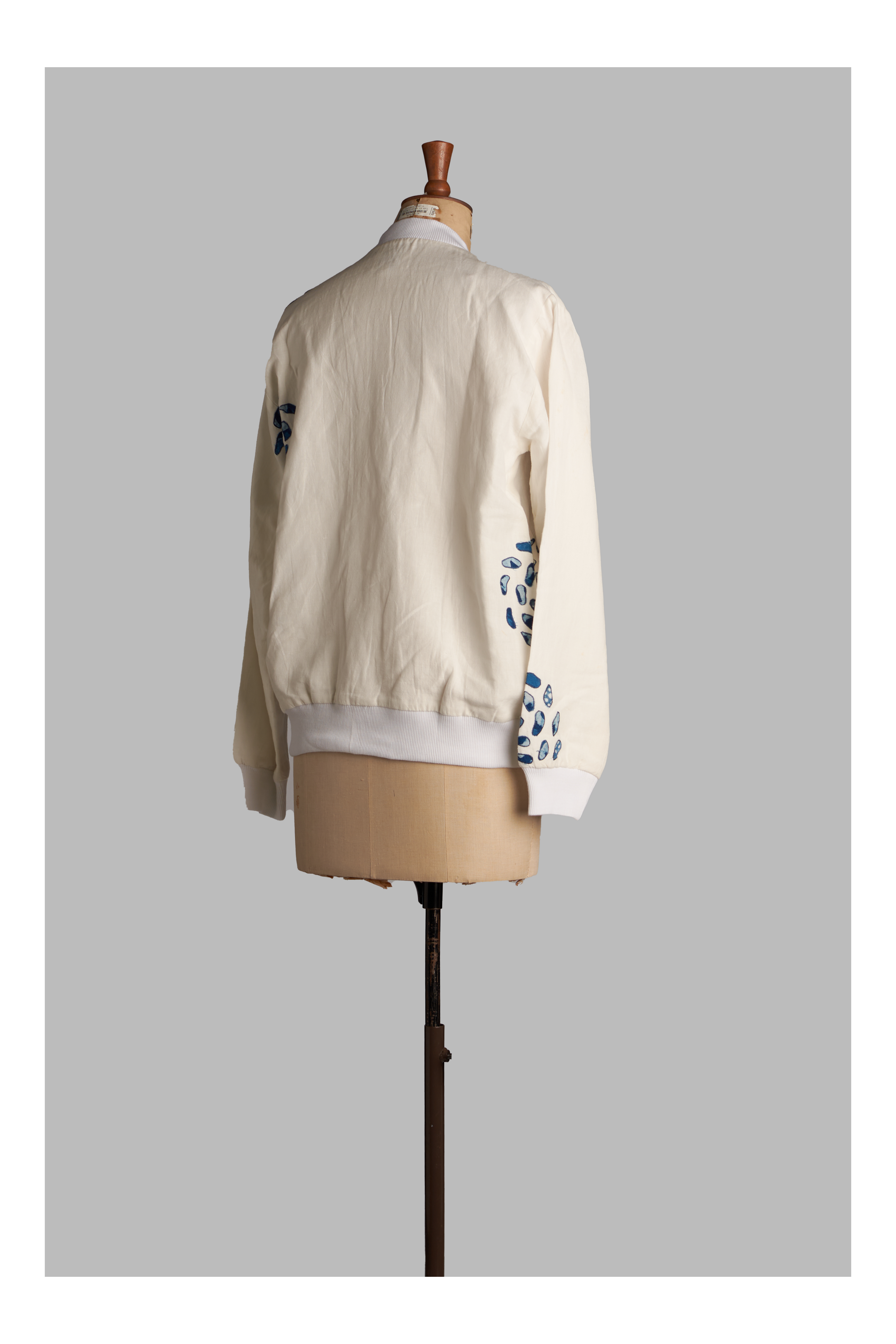 White jacket with floral patterns on sleeves displayed on a mannequin against a gray background