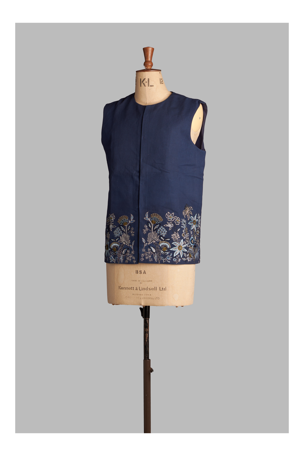 Navy blue vest with floral embroidery on a mannequin against a gray background