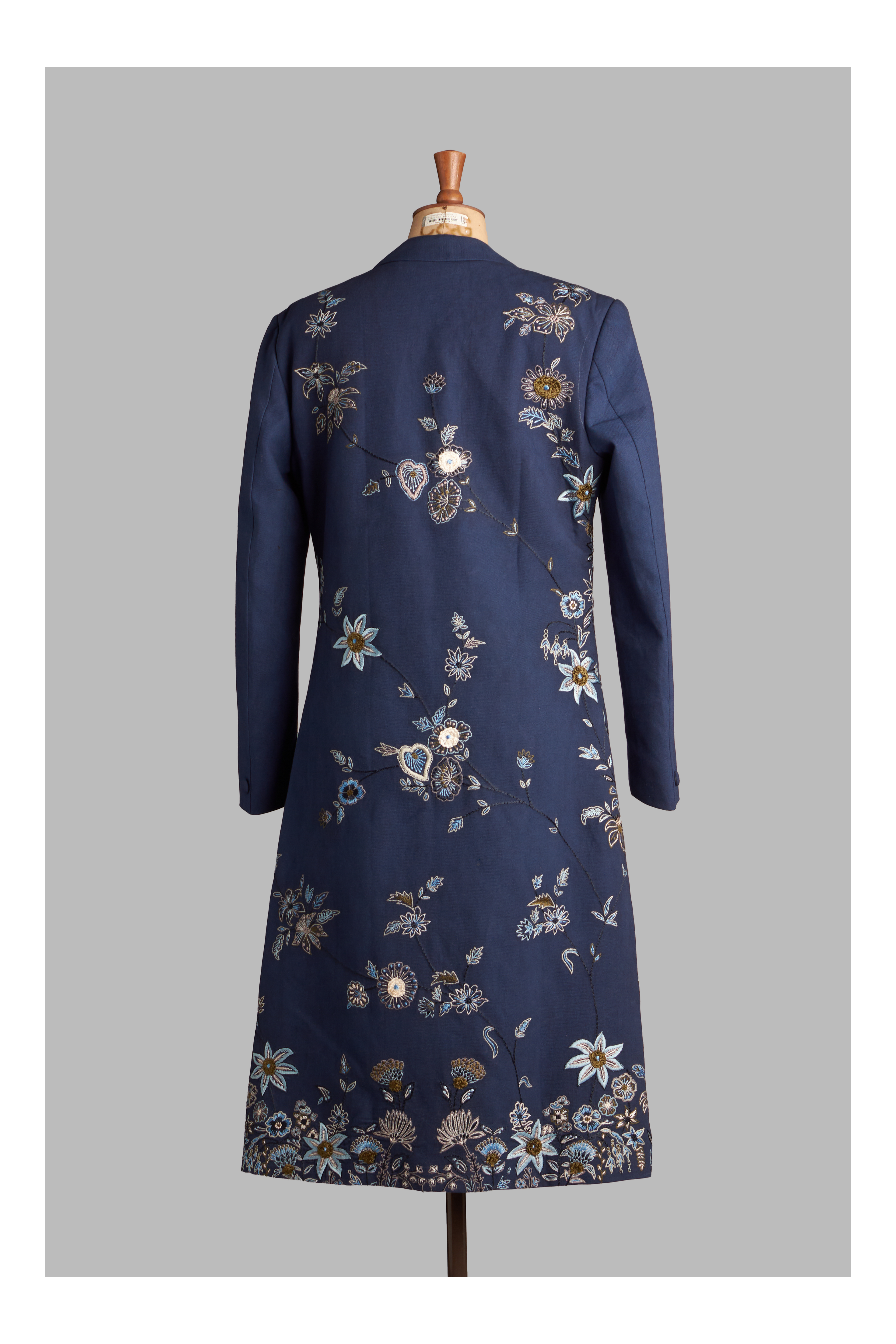 Navy blue long coat with floral embroidery on a mannequin against a gray background